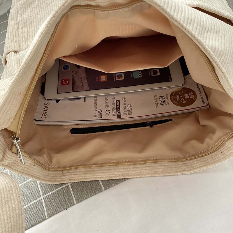 Open beige corduroy Fitlybuy crossbody bag filled with a tablet and magazine on a checkered surface.