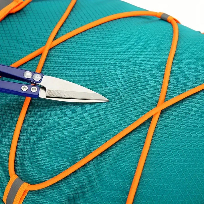 Close-up of a teal Fitlybuy waterproof bike backpack with orange bungee cords and metal fabric scissors testing quality.