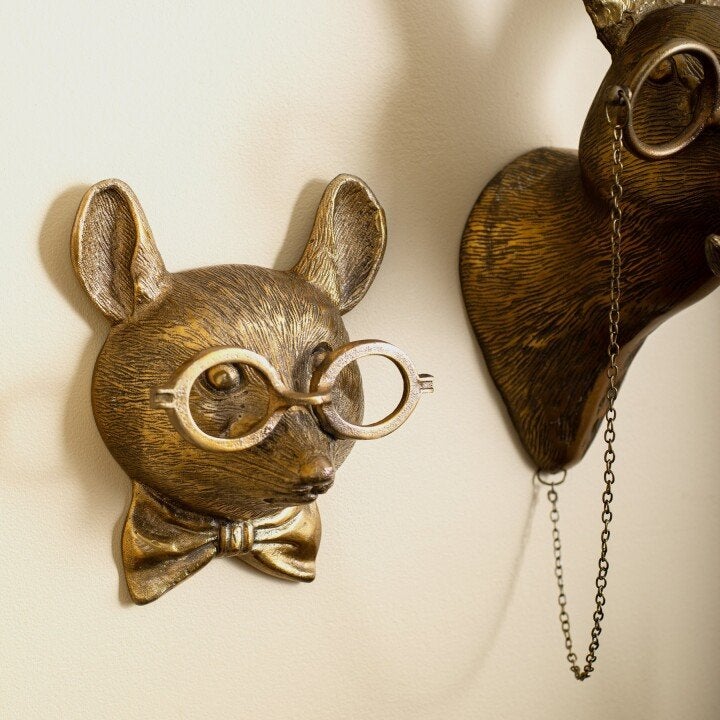 Antique gold-colored mouse wall decor wearing glasses and a bowtie, displayed on a neutral wall.