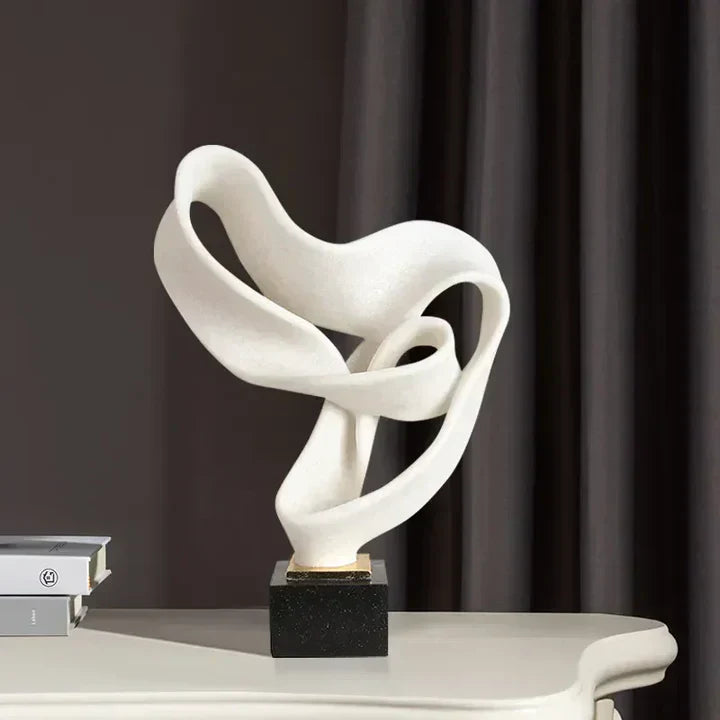 White abstract resin sculpture with a looping ribbon design on a black pedestal, displayed on a desk with books.
