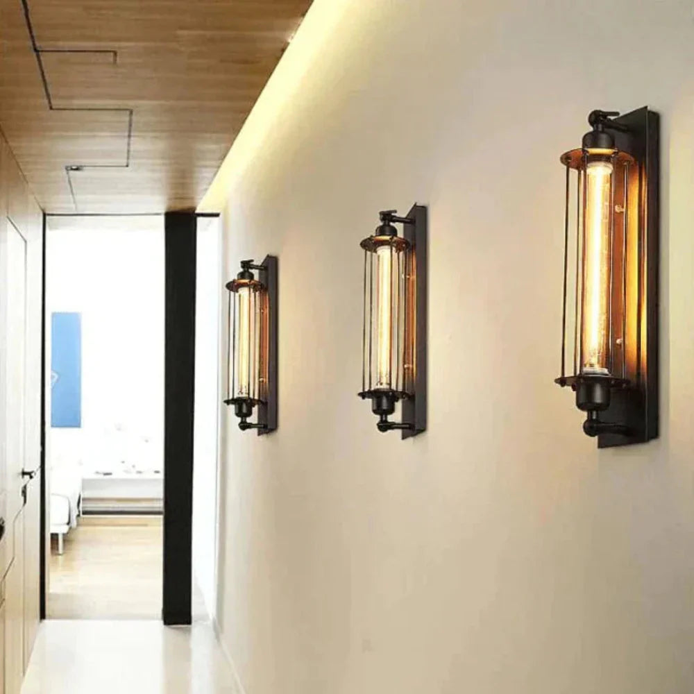 Three vintage wall-mounted LED lights with matte black cages installed in a warm-lit hallway.