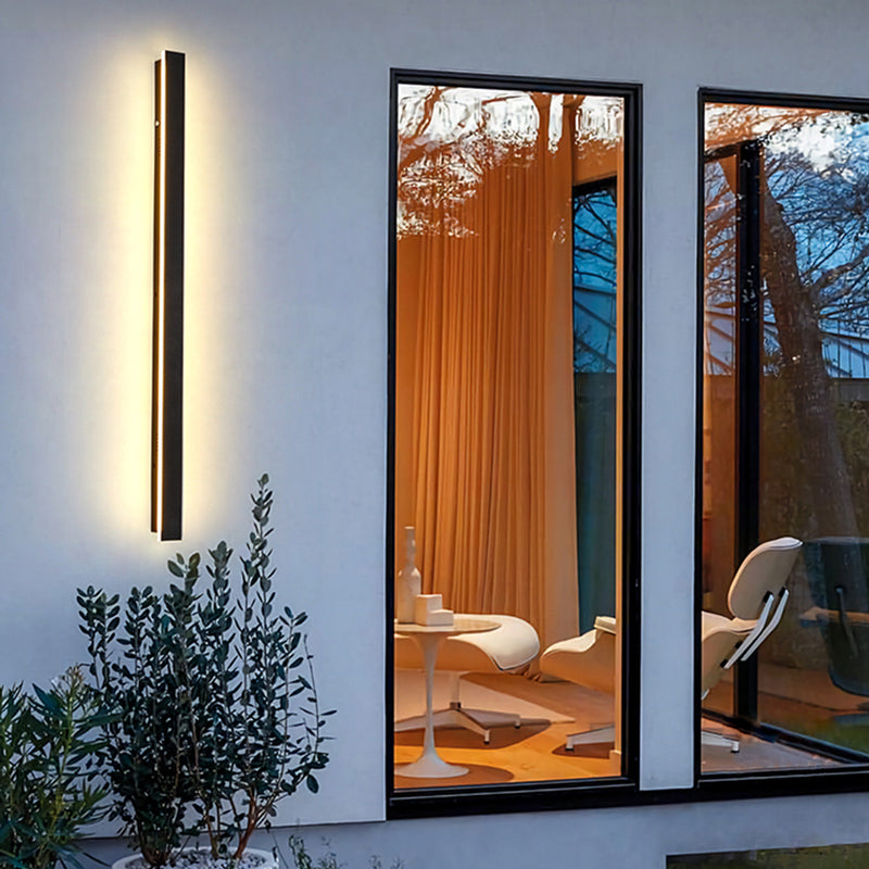 Fitlybuy modern black waterproof LED wall light casting a warm glow on an outdoor wall near windows.
