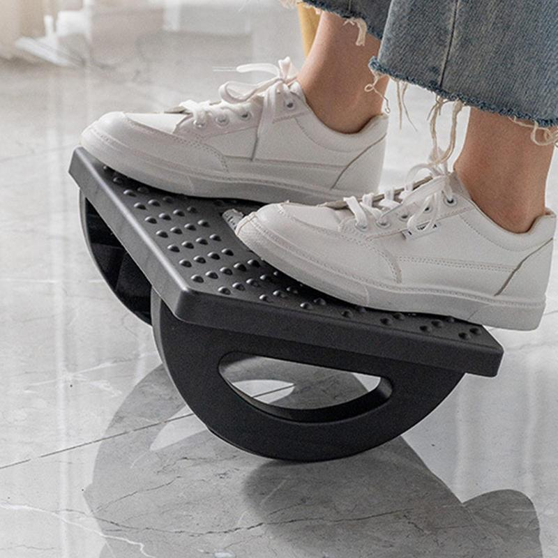 Black ergonomic rocker footrest stool with a textured, studded surface for feet, shown in use on a marble-style floor.