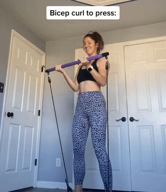Woman performing bicep curls with a purple Fitlybuy Pilates bar and black adjustable resistance bands at home.