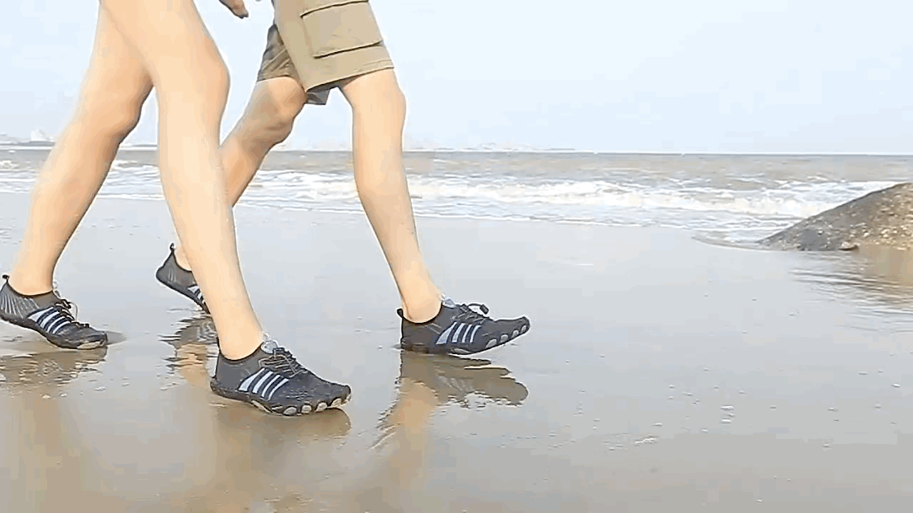 People walking on a beach wearing black Fitlybuy non-slip barefoot shoes with flexible FlexiGrip soles.