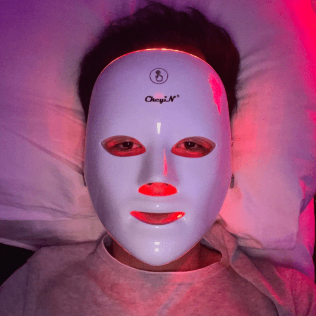 Person lying down wearing a white Fitlybuy LED red light therapy mask, glowing with red light around eyes and mouth.