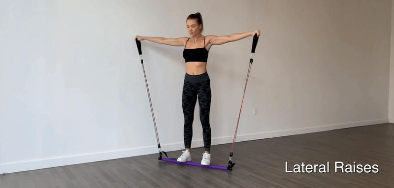 Woman doing lateral raises with a purple Fitlybuy Pilates bar and adjustable resistance bands in a bright home studio.