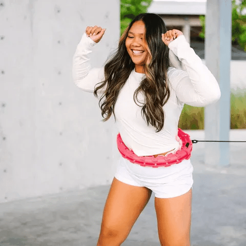 Woman smiling while using a pink Fitlybuy FunFit weighted hula hoop with resistance cord in an outdoor setting.