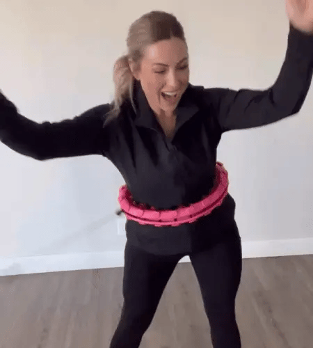 A woman in black activewear exercises with a pink Fitlybuy FunFit weighted hula hoop with CoreFlex resistance.