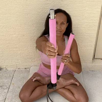 Woman sitting cross-legged holding a pink Fitlybuy Pilates bar with an adjustable resistance system.