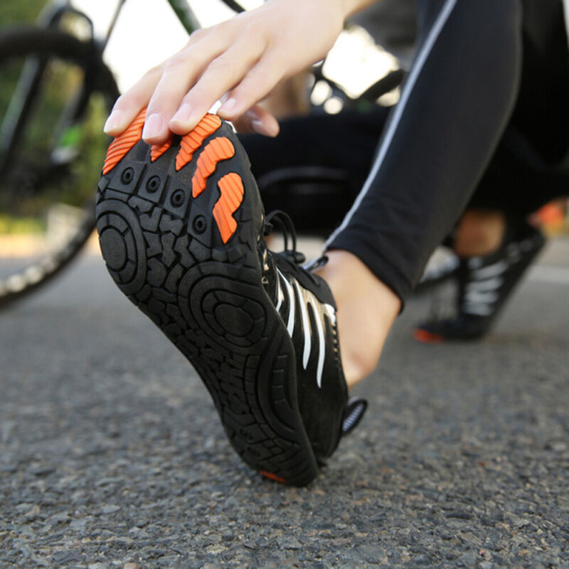 Fitlybuy non-slip black barefoot shoes with orange FlexiGrip soles held by a person on an outdoor bike path.