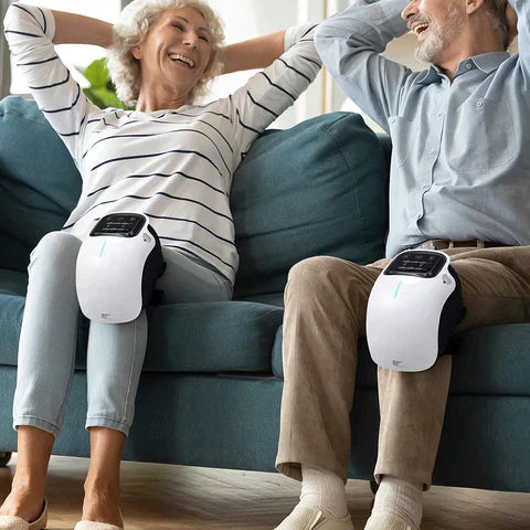 Couple sitting on a sofa wearing white Fitlybuy infrared heated knee massagers for soothing therapy.