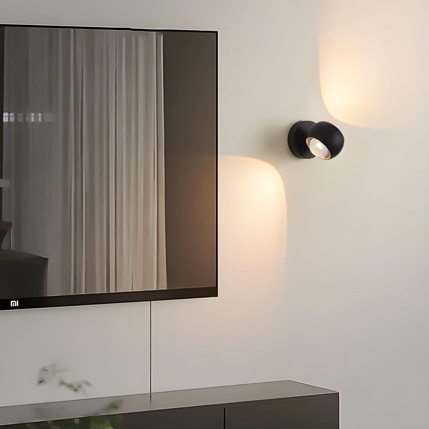 Matte black Fitlybuy ModernEdge rotating LED wall light mounted next to a TV, casting a warm glow on a white wall.