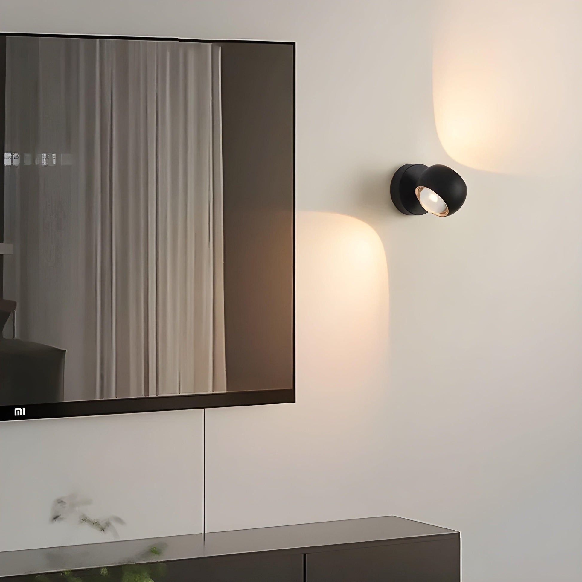 Matte black Fitlybuy ModernEdge rotating LED wall light mounted next to a TV, casting a warm glow on a white wall.