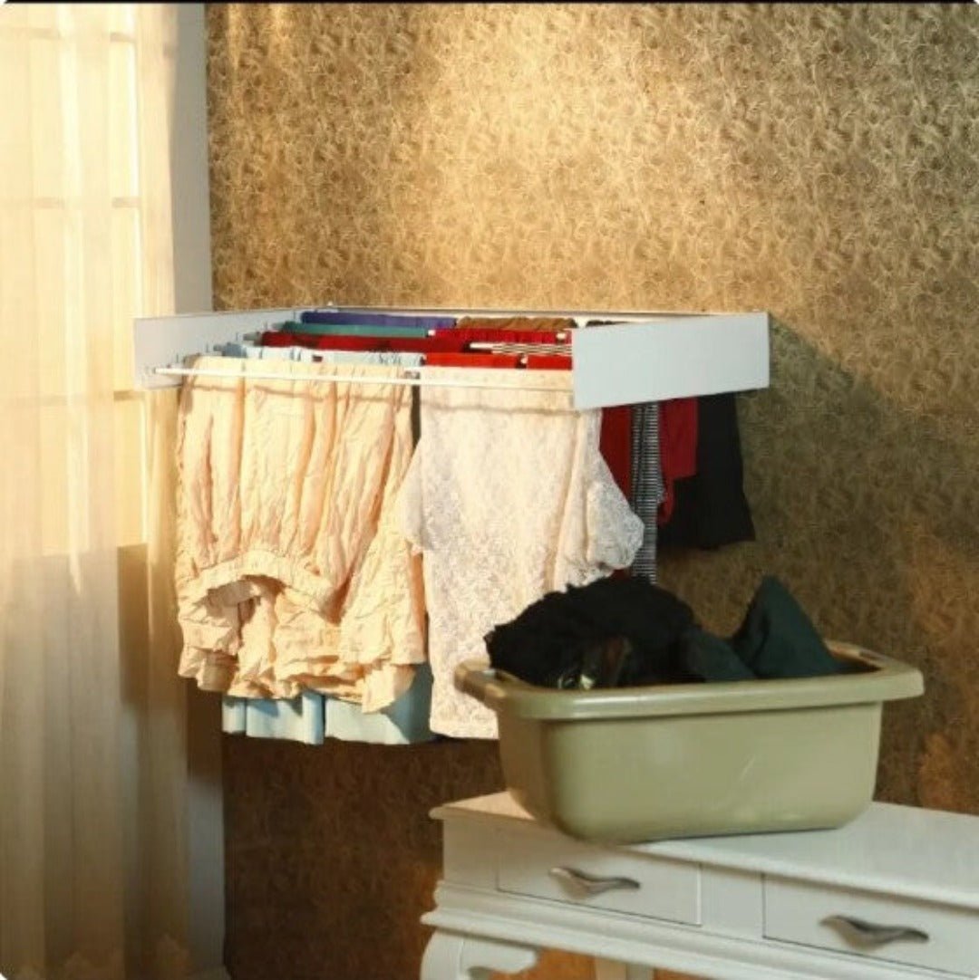 Fitlybuy white, foldable wall-mounted drying rack holding hanging laundry with a clothes basket on a white table nearby.