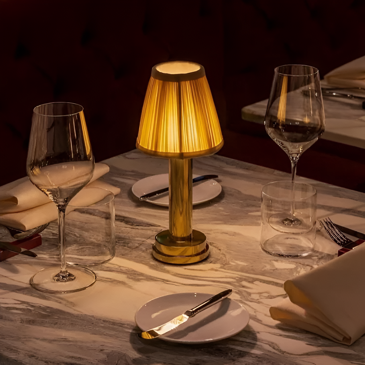 Fitlybuy vintage gold aluminium table lamp with a glowing pleated fabric shade, set on a marble restaurant table.