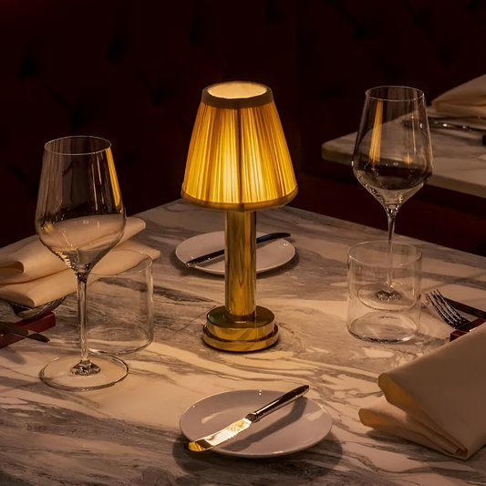 Fitlybuy vintage gold aluminium table lamp with a glowing pleated fabric shade, set on a marble restaurant table.