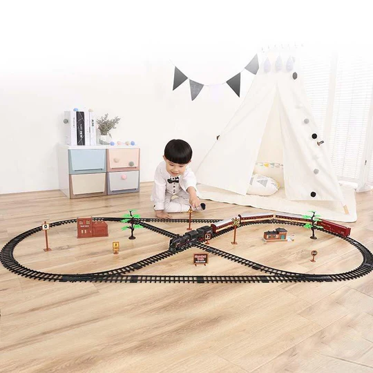 Child playing with a Fitlybuy 39-piece HO scale black train set on an oval track with model buildings and trees.