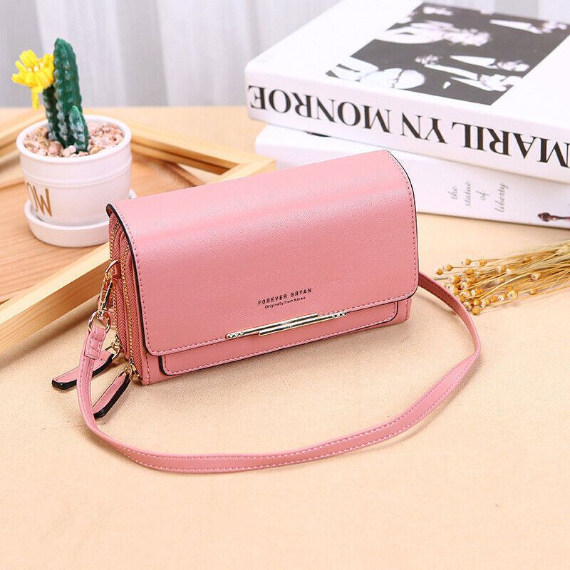 Pink Fitlybuy leather crossbody bag with dual zippers, gold trim, and thin shoulder strap on a desk with decor.