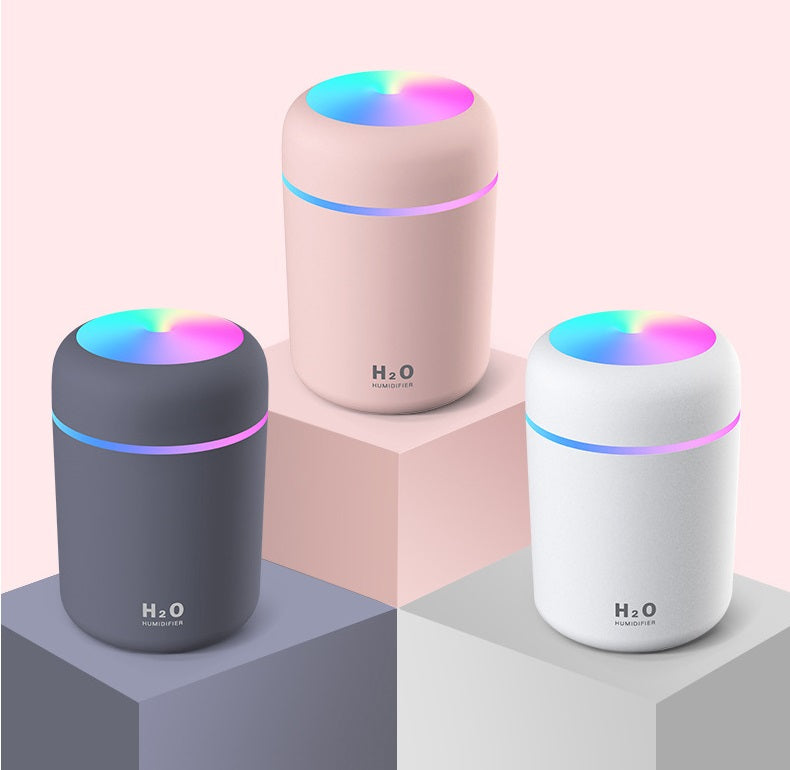 Three Fitlybuy portable aroma air diffusers in gray, pink, and white with illuminated colorful LED tops on podiums.