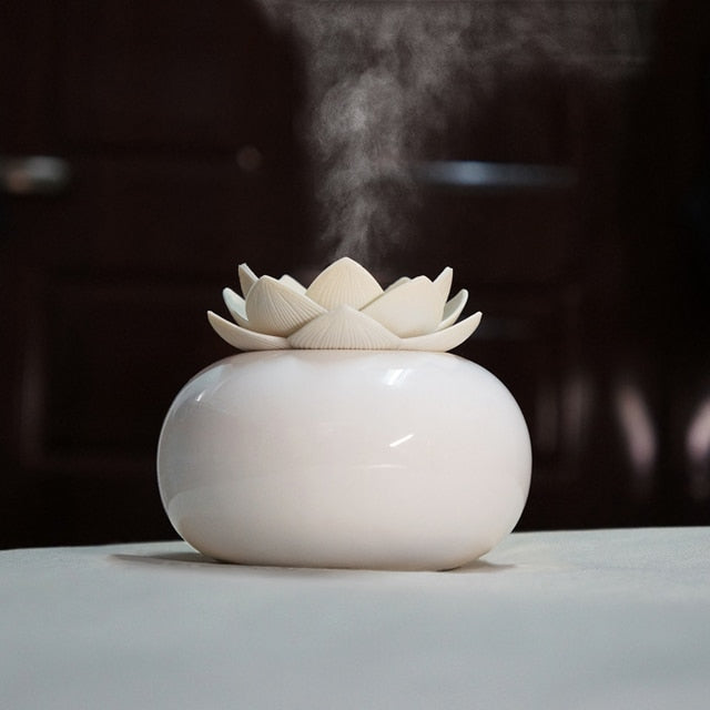 White ceramic Lotus aroma humidifier diffusing mist via ultrasonic technology on a table against a dark background.