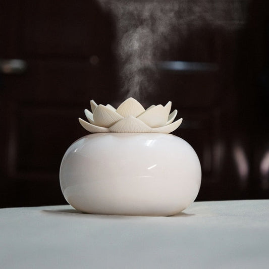 White ceramic Lotus aroma humidifier diffusing mist via ultrasonic technology on a table against a dark background.