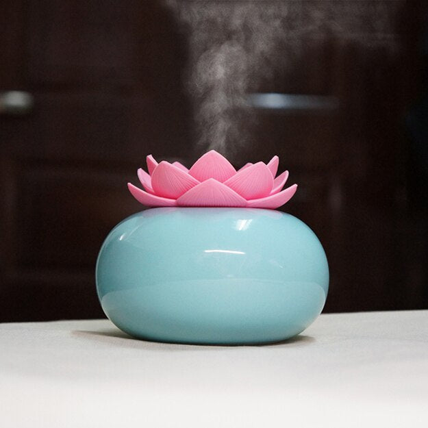 Fitlybuy blue ceramic lotus essential oil diffuser with a pink flower top releasing a fine mist on a table.