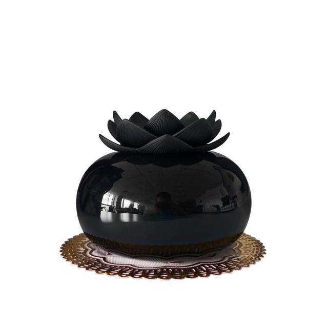 Glossy black ceramic lotus-shaped aroma humidifier with ultrasonic diffusion technology on a gold decorative lace doily.