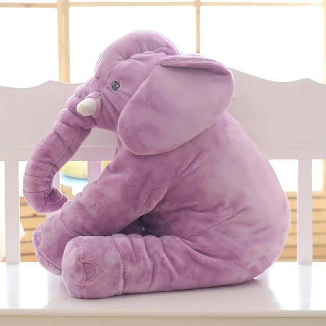 Plush purple elephant pillow for kids. Soft, cuddly stuffed animal sitting on a white bench near a window.