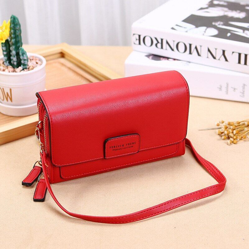 Red Fitlybuy premium leather crossbody bag with a front flap, dual zippers, and strap on a table with decor.