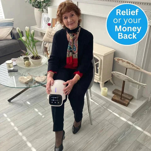 Woman using a white Fitlybuy infrared heated knee massager with digital display in a cozy living room setting.