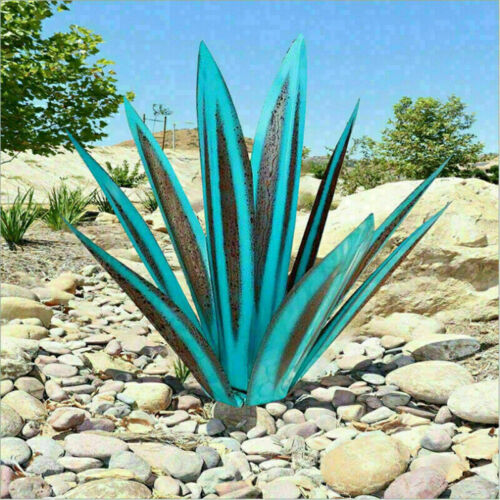 Teal and rust metal agave garden sculpture placed outdoors on a rock-filled landscape under a clear blue sky.