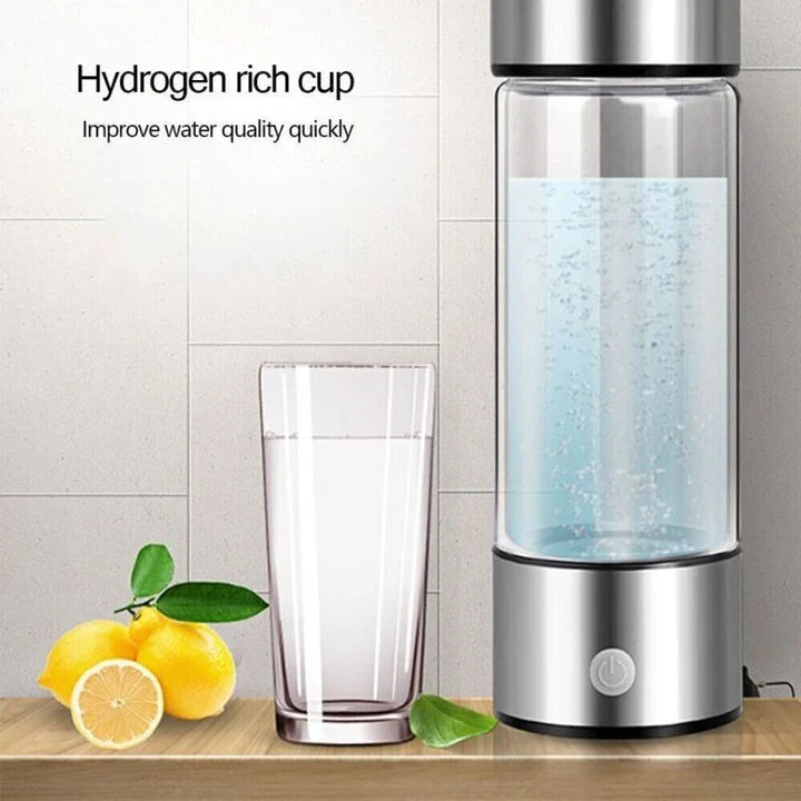 Fitlybuy silver hydrogen water generator bottle with bubbles, beside a glass of water and lemons on a wooden table.