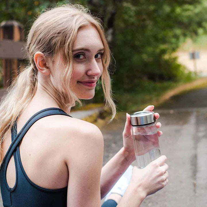 Woman holding a clear Fitlybuy hydrogen water bottle with a silver lid while exercising outdoors.