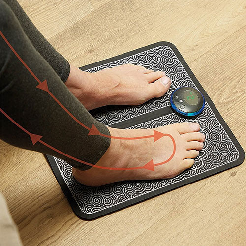 Black-and-white patterned Fitlybuy EMS foot massage mat with control unit, being used by bare feet on a wooden floor.