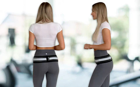 Woman in a gym wearing a black and white Fitlybuy Sciatica Relief Belt over grey leggings for hip support.