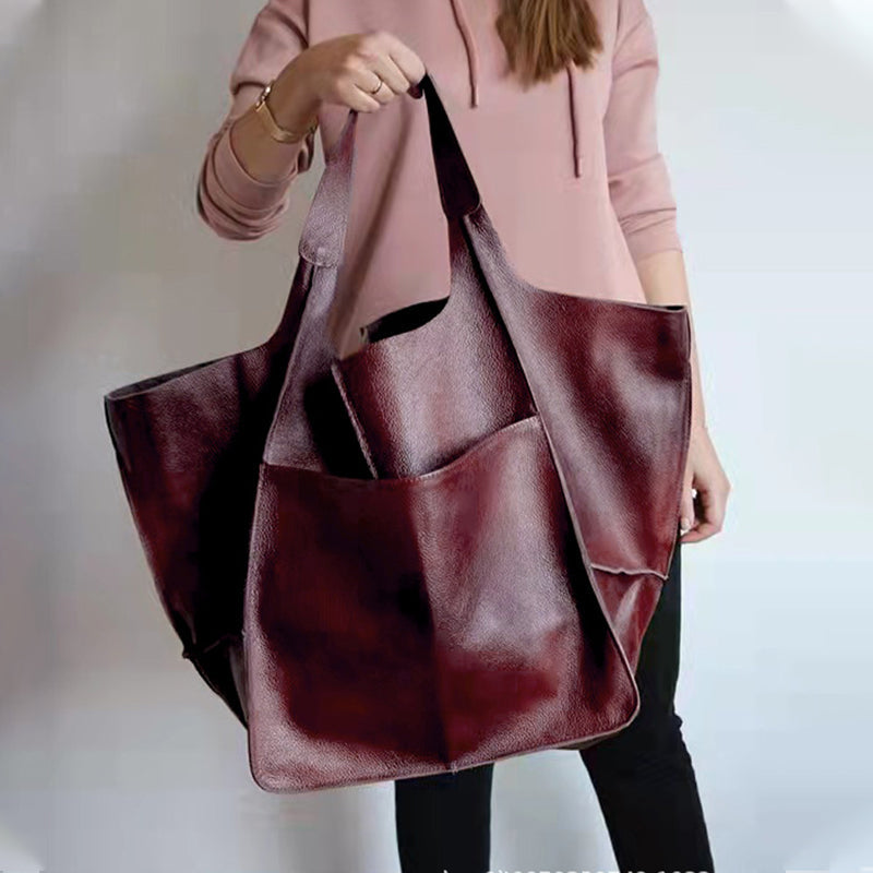 Woman wearing a pink hoodie holding a large, burgundy pebbled leather tote bag with an exterior pocket.