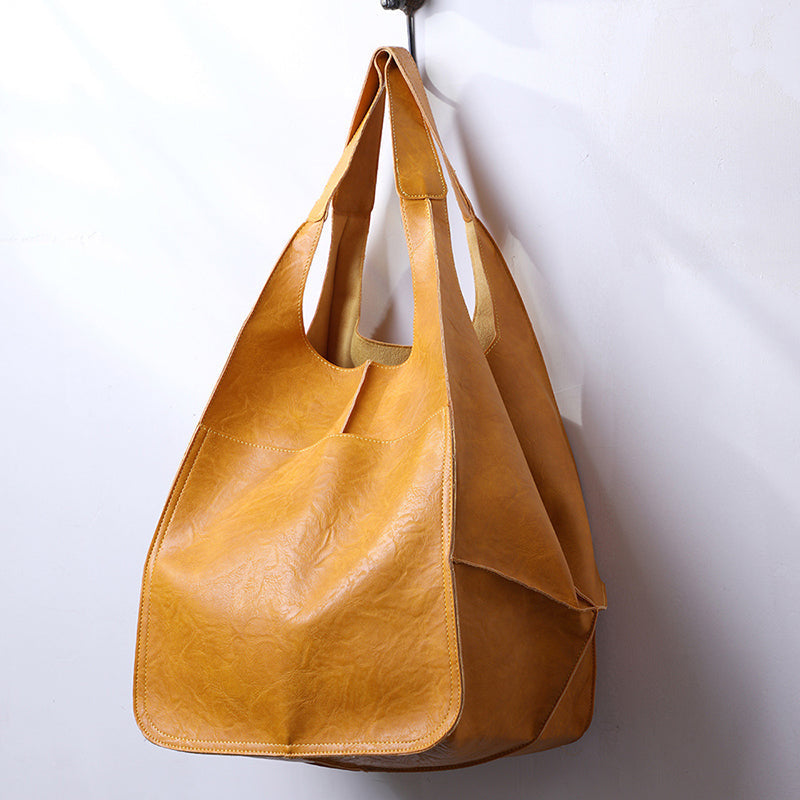 Fitlybuy oversized mustard yellow leather weekender tote bag with wide straps, hanging against a white wall.