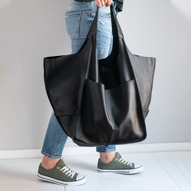 Fitlybuy oversized black leather weekender bag carried by a person in blue jeans and olive green sneakers.