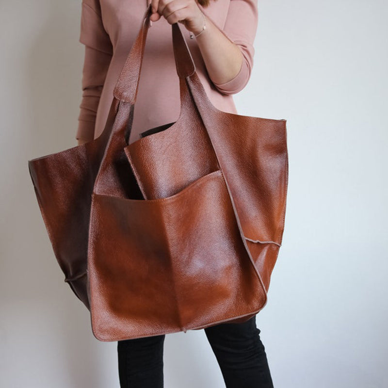 Person holding a large, brown leather Fitlybuy oversized weekender tote bag with wide carry handles.