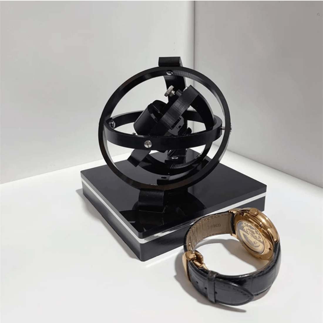 Fitlybuy black luxury automatic watch winder with a 3D orbital design, displayed next to a gold and leather watch.