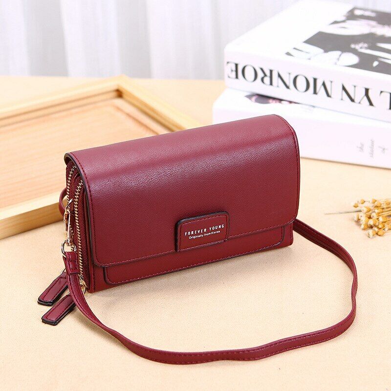 Fitlybuy burgundy leather crossbody bag with dual-zipper closure and "Forever Young" emblem, on a beige desk.