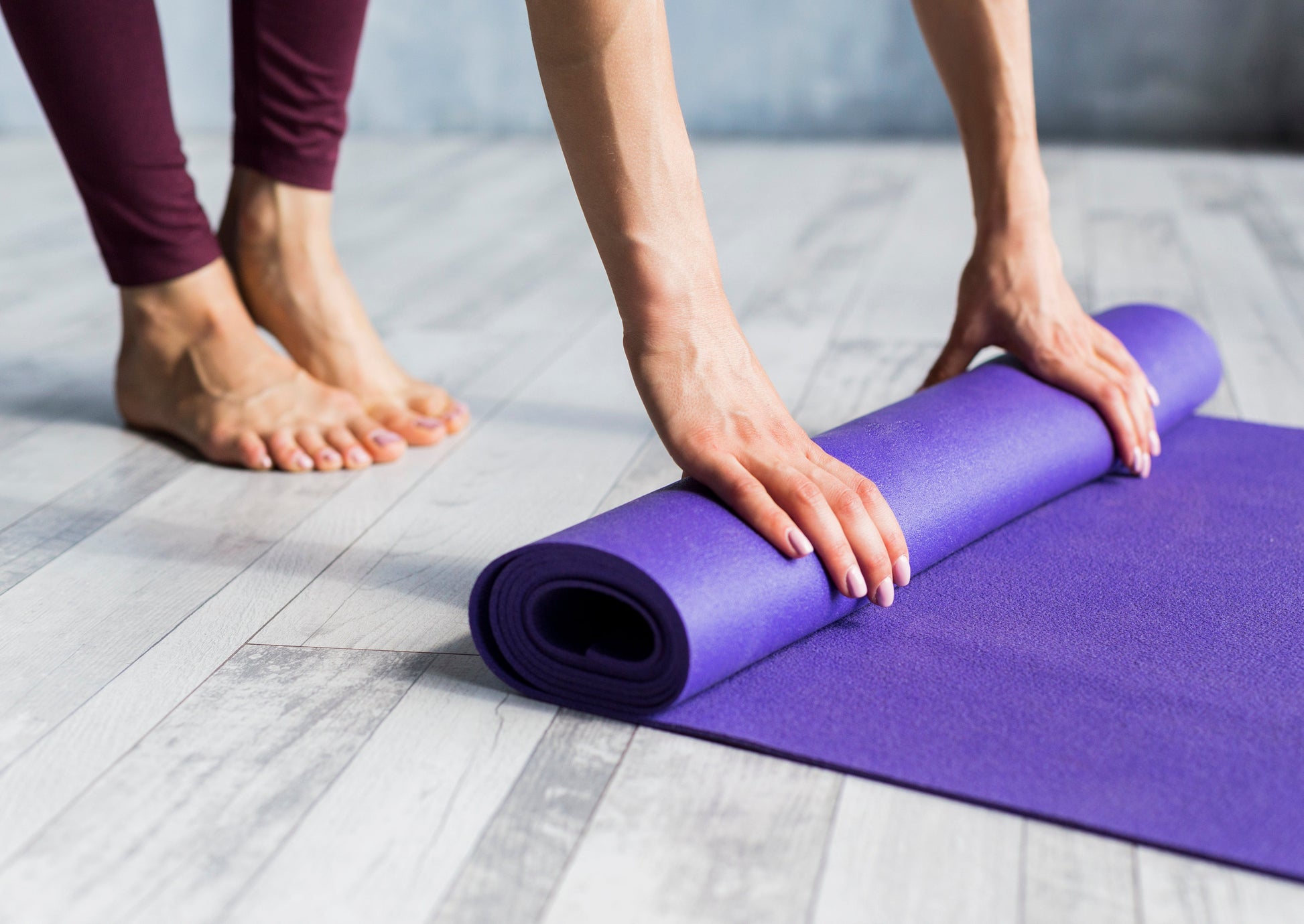 Fitlybuy 6mm purple yoga mat with EcoGrip non-slip surface being rolled up by a person on a wooden floor.