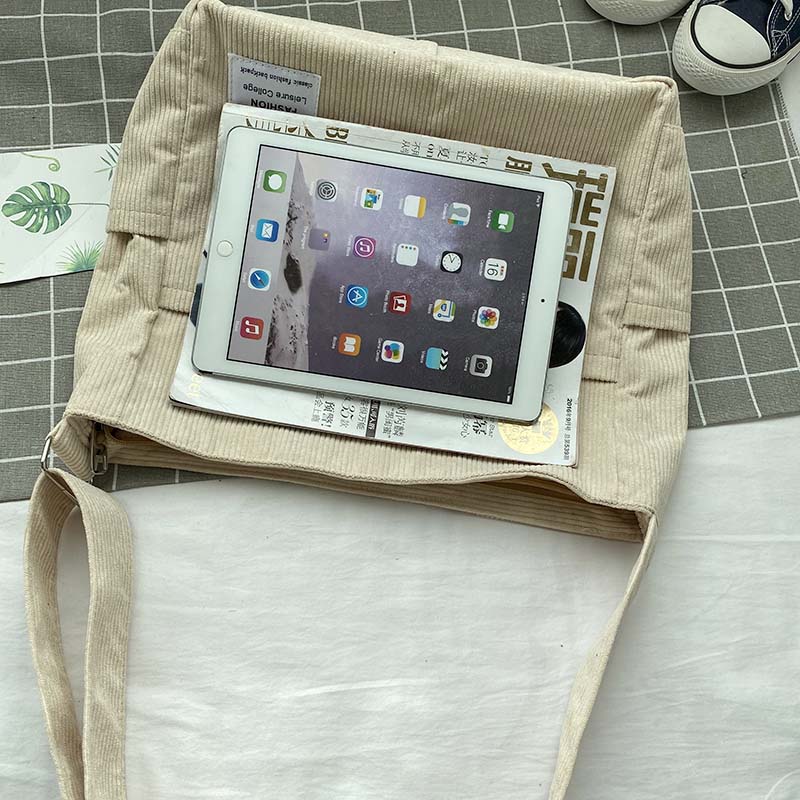 Beige corduroy Fitlybuy crossbody bag holding a magazine and tablet on a checkered surface.